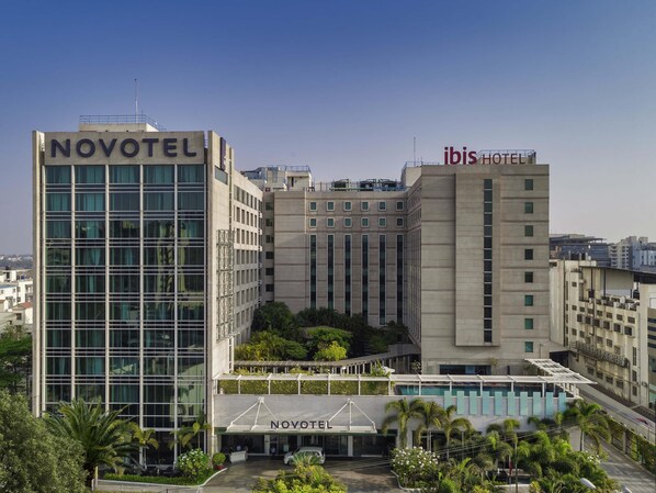 Un hôtel Novotel doté d’une façade moderne en verre, d’un jardin sur le toit et d’une entrée bien visible.