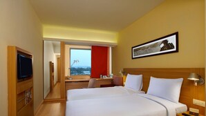 A hotel room with a large bed, a desk, a television, and a window with a view. - Ibis Bengaluru Outer Ring Road (Bengaluru)