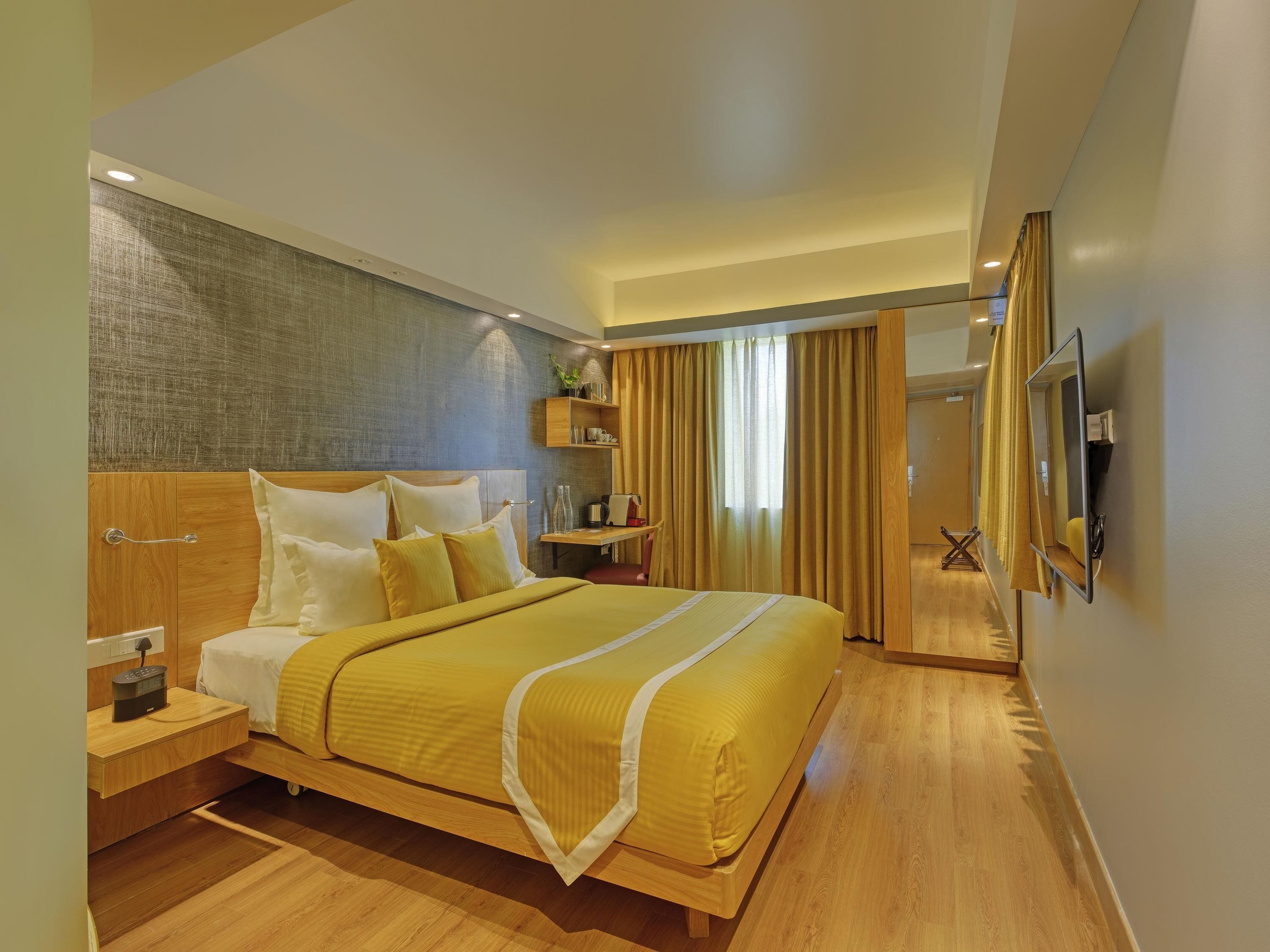 A modern hotel room with a wooden bed, bedside tables, a TV, and a large window with curtains.