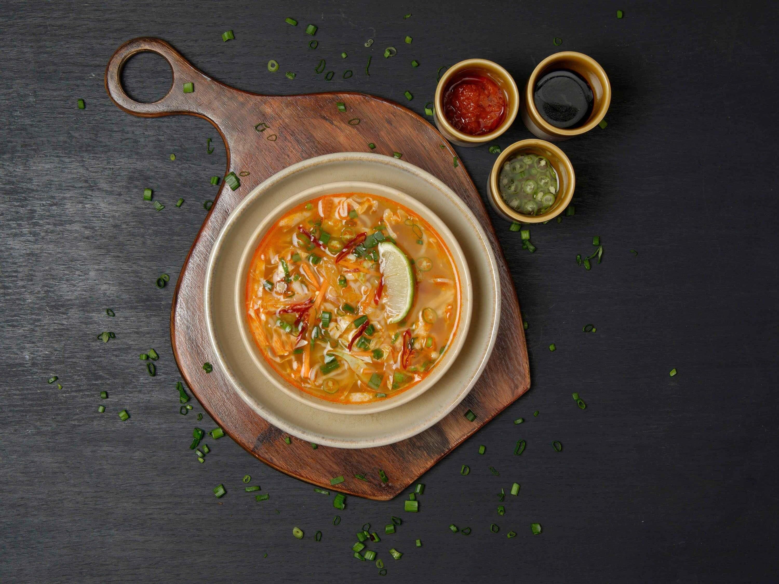 A bowl of soup with garnishes on a wooden board.