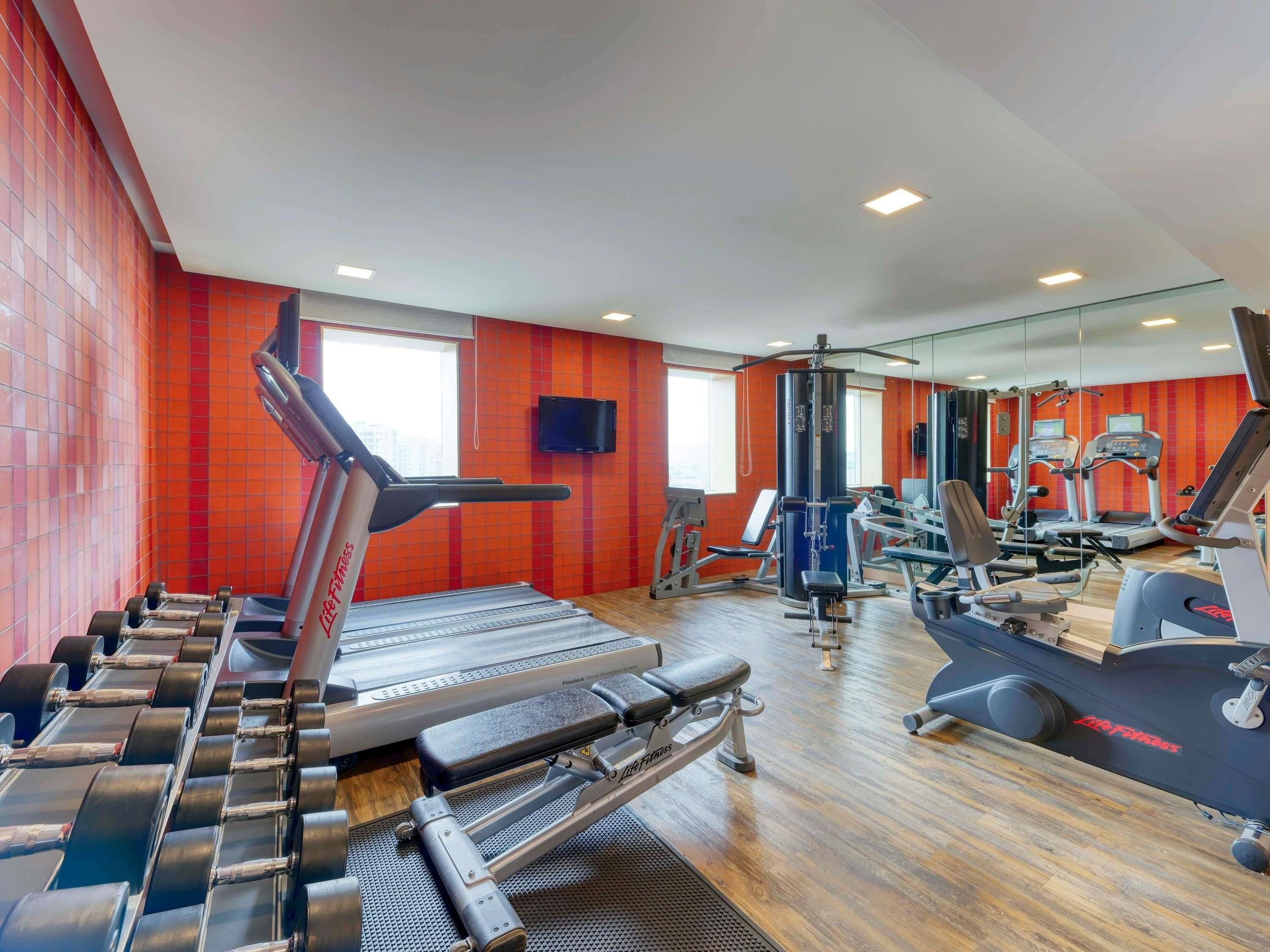 Une salle de sport équipée de tapis de course, d’appareils de musculation et d’un mur recouvert de miroirs.