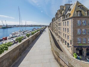 Una passeggiata lungomare con una fila di edifici, un porto turistico con barche e un cielo sereno.