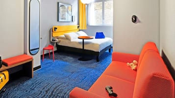 Quarto de hotel com uma cama, sofá vermelho, mesa pequena, cadeira, espelho e janela com cortinas.