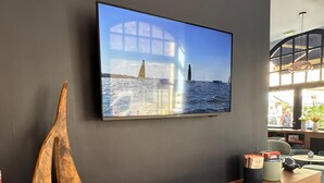 A modern reception desk with a wooden finish, a mounted television displaying a coastal scene, and a sailboat sculpture on the wall. - ibis Styles Saint-Malo Centre Historique (Saint-Malo)