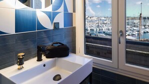 A bathroom with a white sink, a mirror, and a view of a marina through a window. - ibis Styles Saint-Malo Centre Historique (Saint-Malo)
