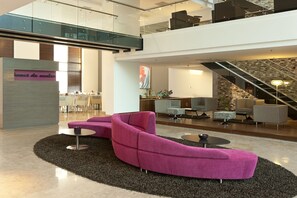 A modern lobby with a curved pink sofa, a small round table, and a staircase. - NH Collection Barranquilla Smartsuites Royal (Barranquilla)