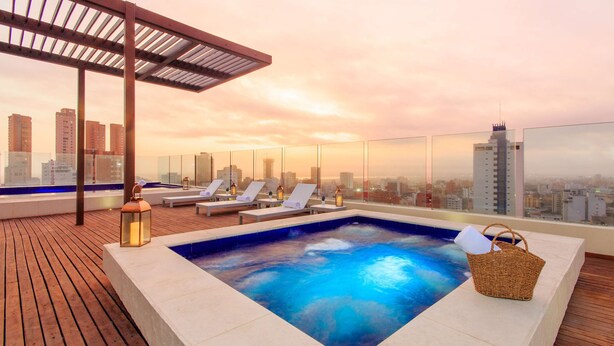 A rooftop pool area with lounge chairs, a hot tub, and a city view at sunset. - NH Collection Barranquilla Smartsuites Royal (Barranquilla)