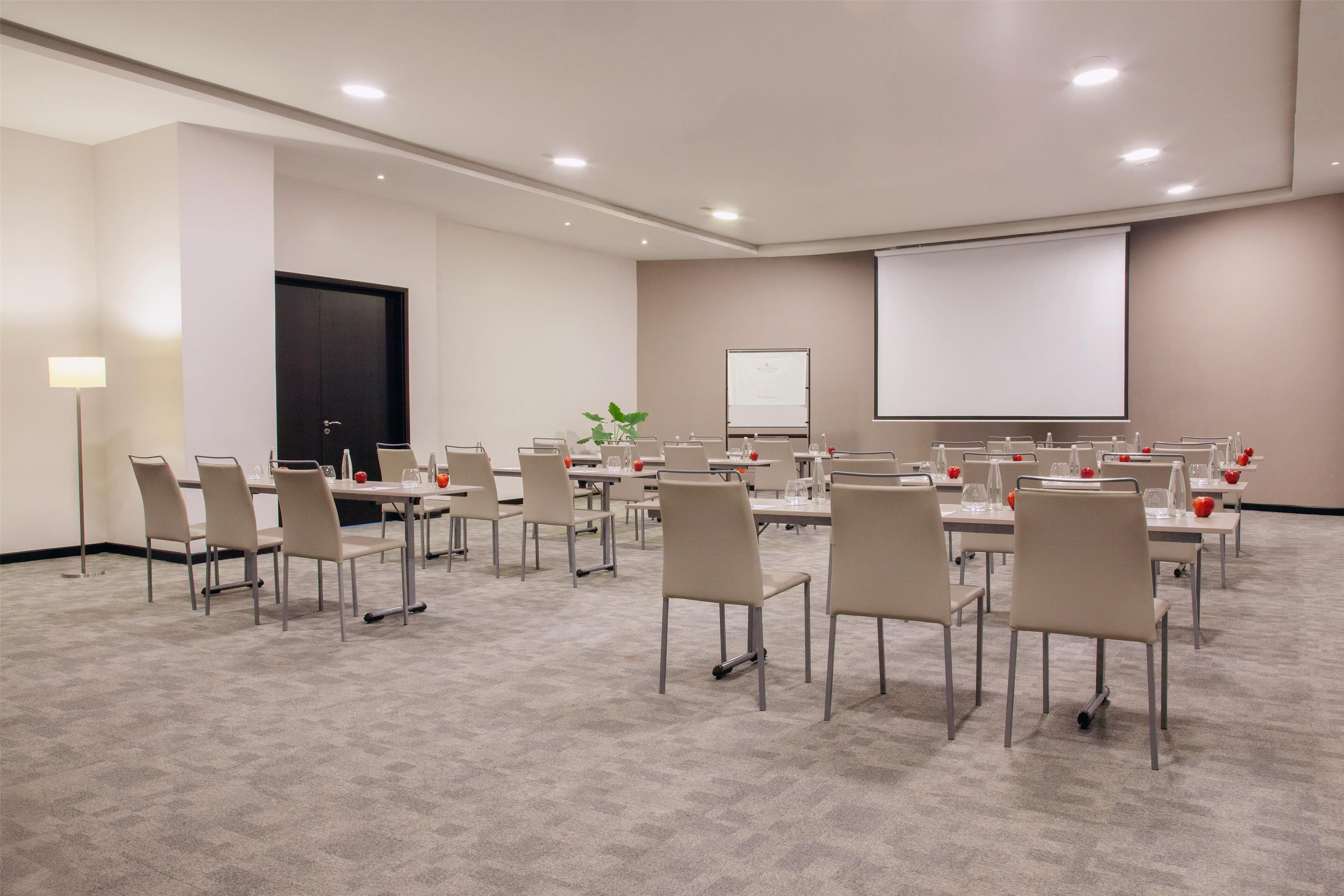 Una sala de conferencias con varias mesas y sillas, una pantalla de proyector y una pizarra.