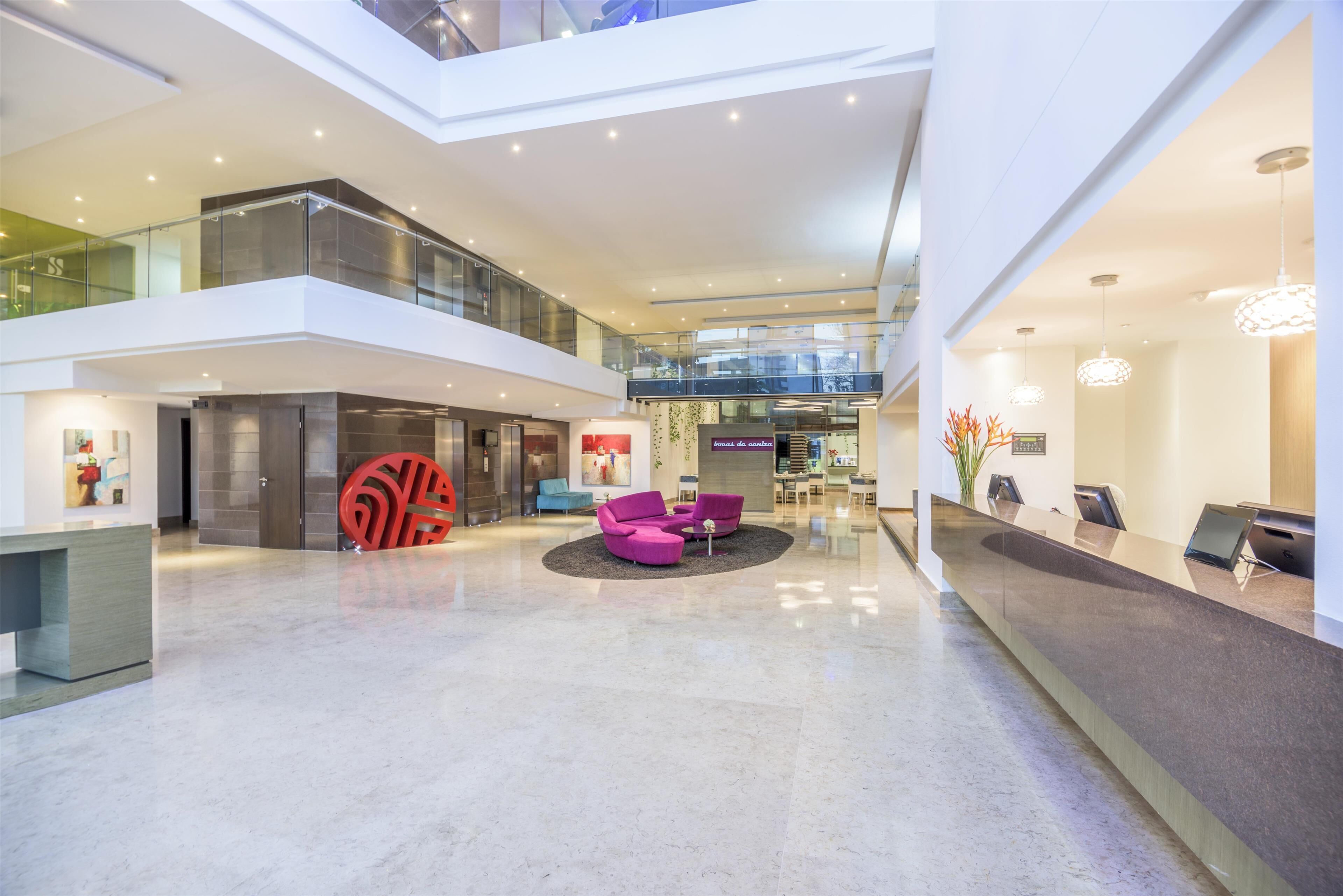 A spacious lobby with a high ceiling, a reception desk, and a seating area with purple chairs.