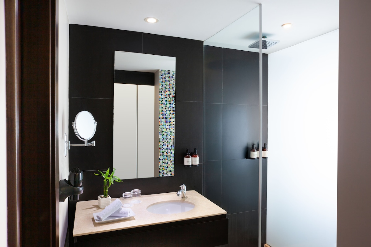 A modern bathroom with a large mirror, two sinks, a hairdryer, and a small plant.