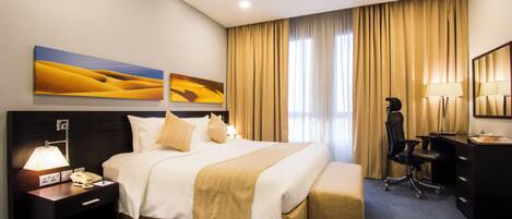 A hotel room with a large bed, a desk, a chair, and two paintings on the wall.