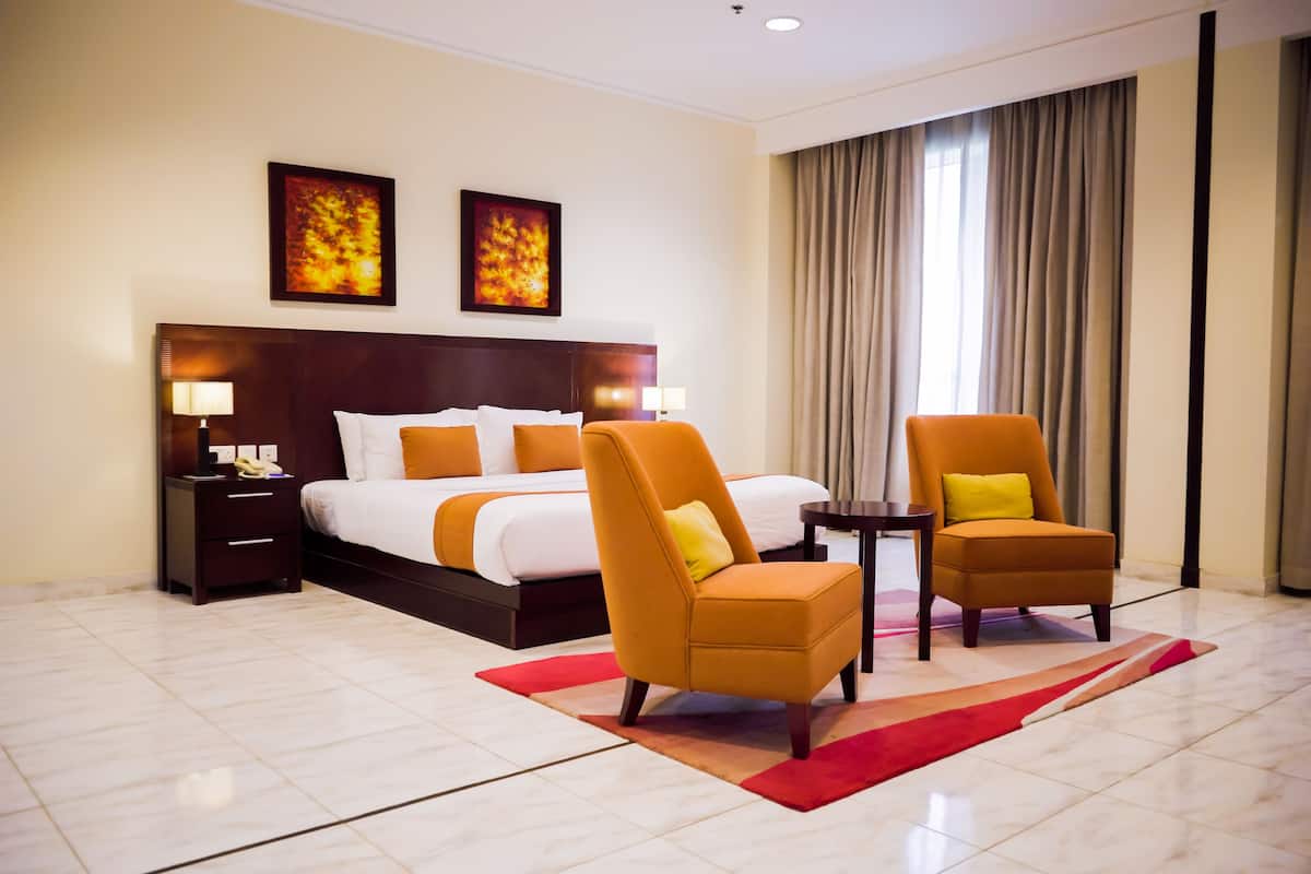 Una habitación de hotel con una cama grande, dos sillones, una mesita de noche y una alfombra roja.