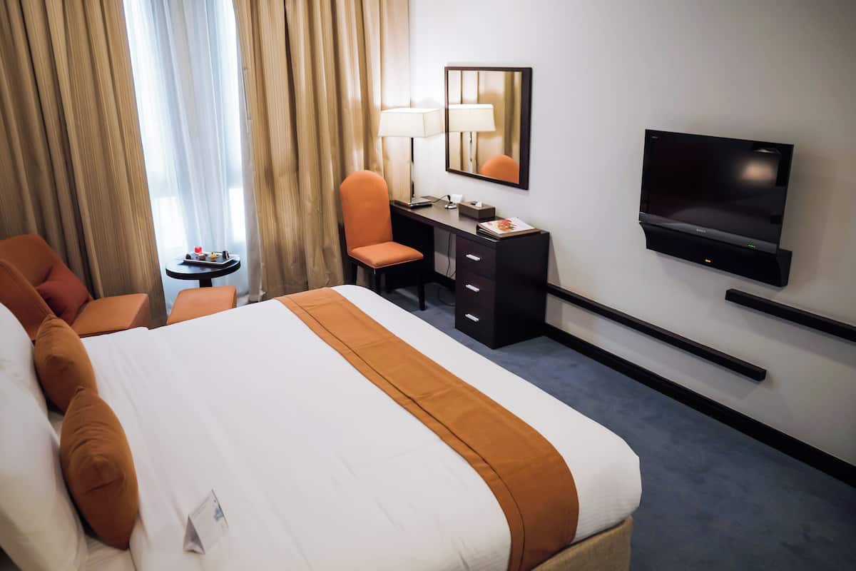 Habitación de hotel con una cama grande, un escritorio, una silla, un televisor y una mesita de noche con lámpara.