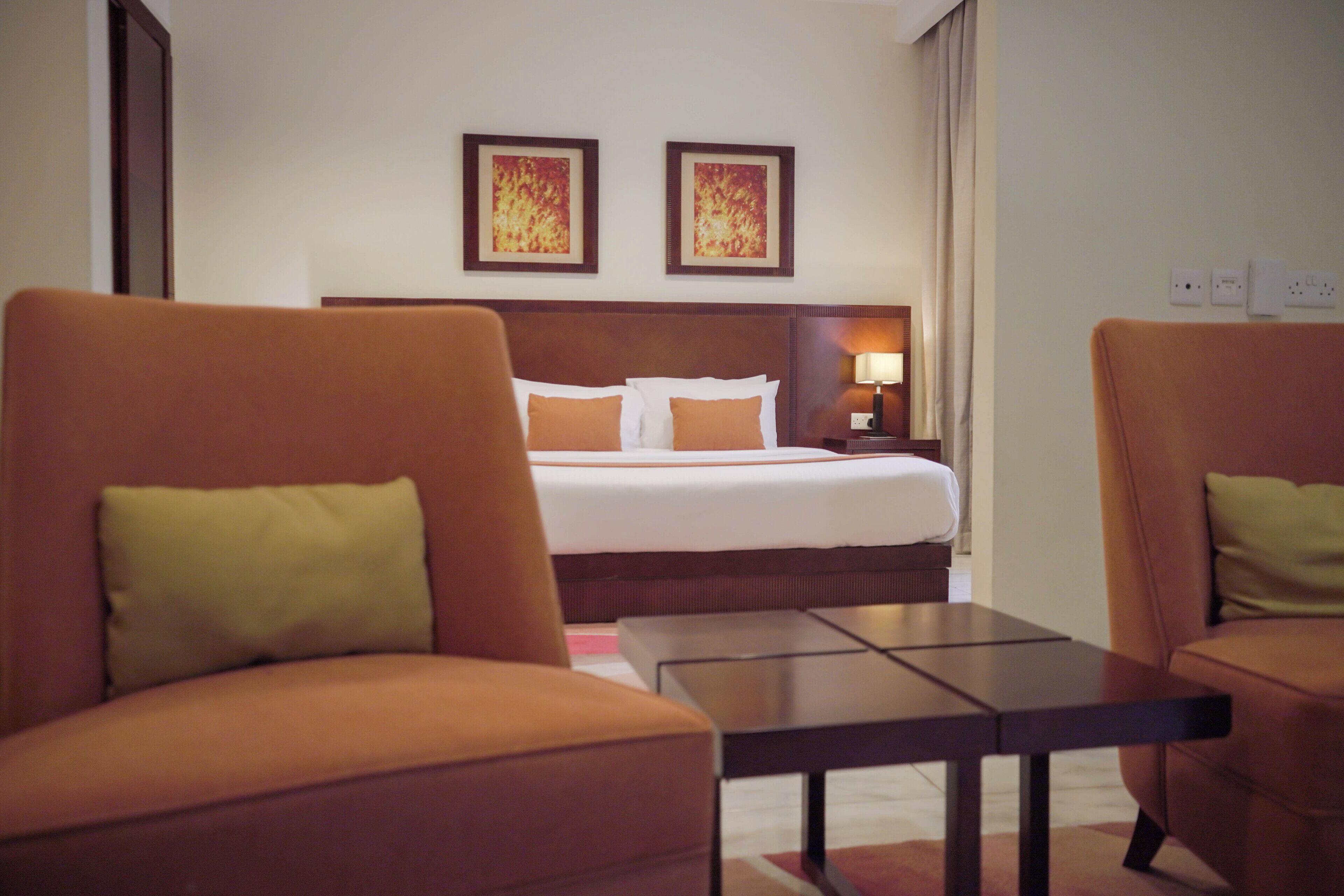 A hotel room with a bed, two armchairs, a small table, and two framed pictures on the wall.