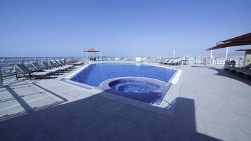 Ein Pool auf dem Dach mit Liegestühlen, einem Whirlpool und freiem Blick auf das Meer.