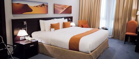 Habitación de hotel con una cama grande, una mesita de noche con lámpara, una silla y una obra de arte en la pared.