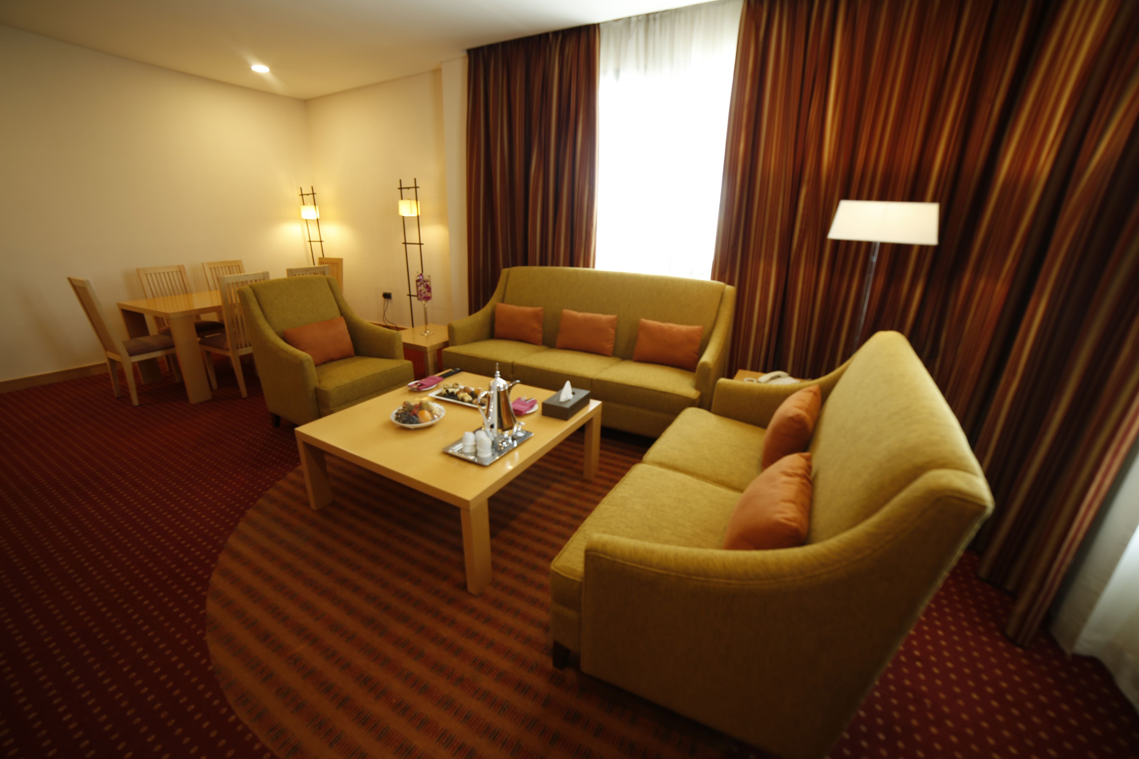 A hotel room with a sofa, armchairs, a coffee table, and a dining area.