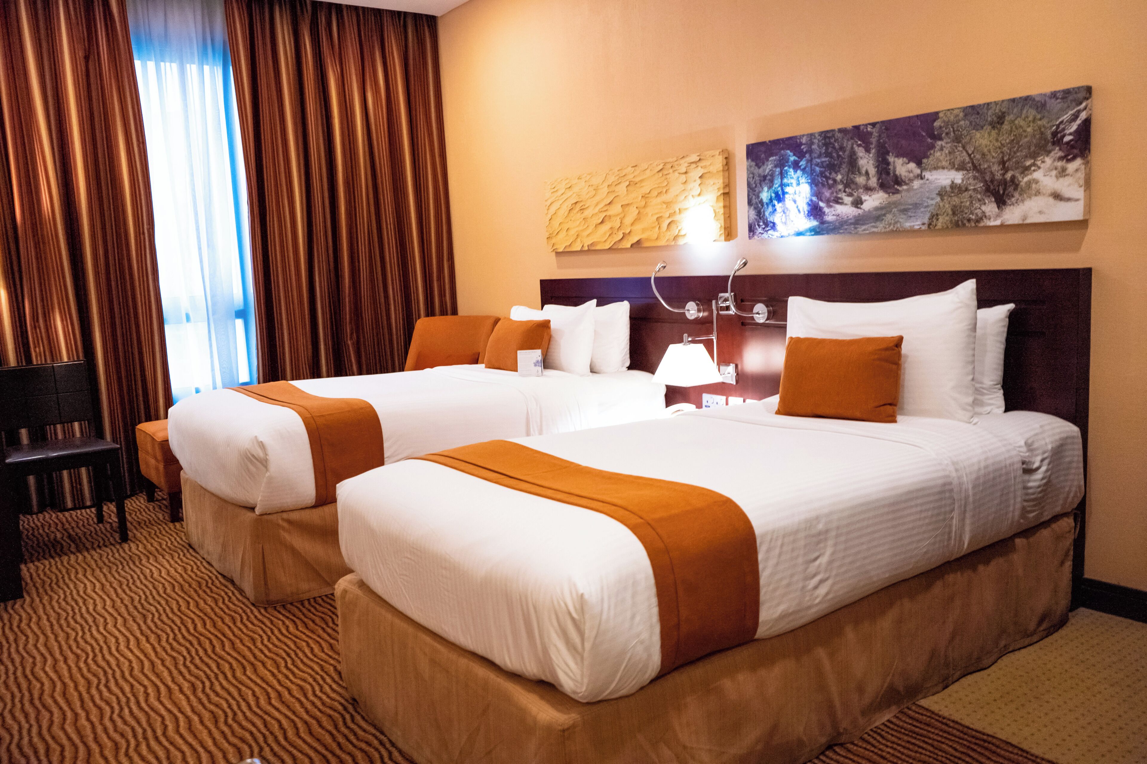 Una habitación de hotel con dos camas, un escritorio y un ventanal grande con cortinas.