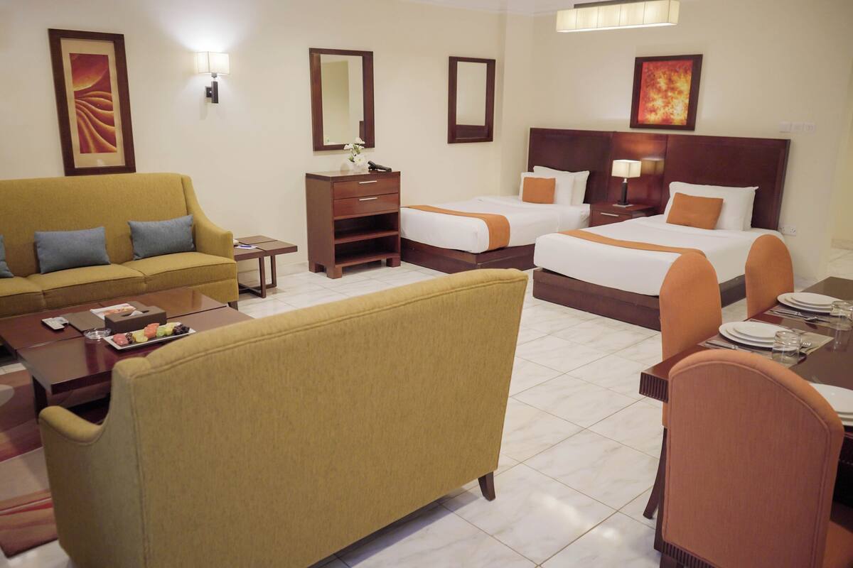 Una habitación de hotel con sofá, dos camas individuales, una mesa de comedor y un escritorio pequeño.