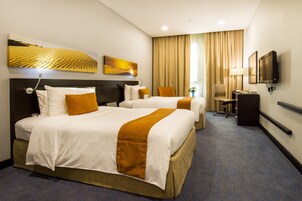 A hotel room with two beds, a desk, a chair, a TV, and artwork on the walls.
