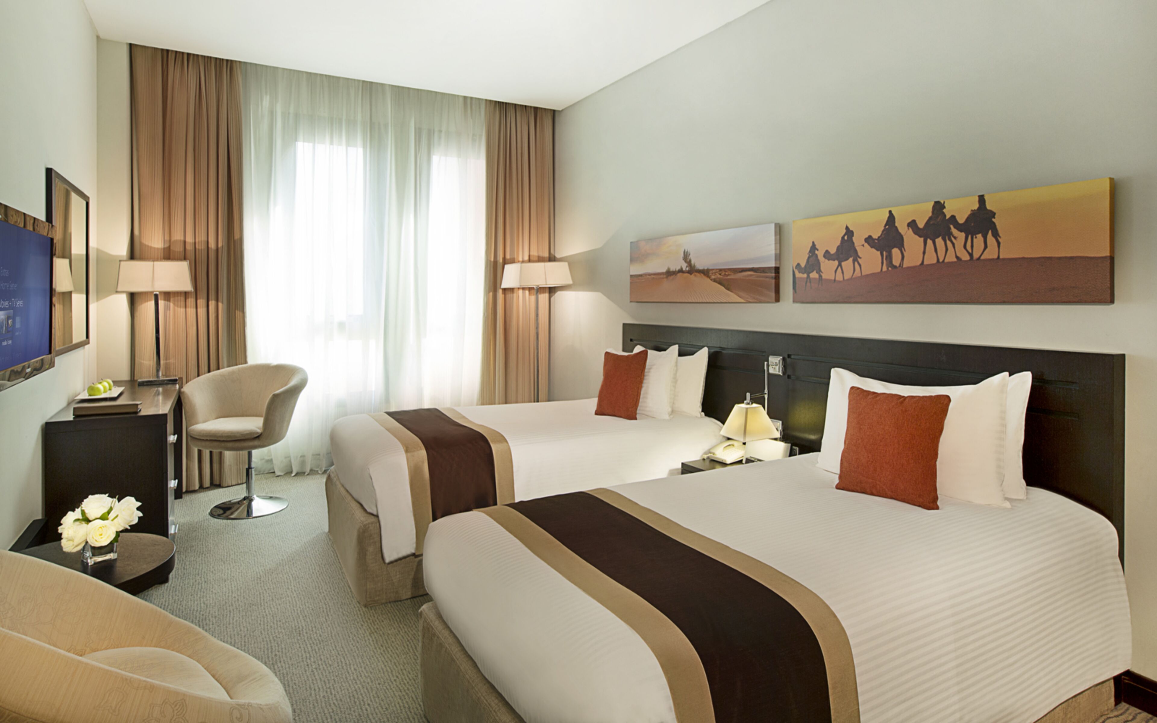 A hotel room with two beds, a desk, a chair, and a TV.