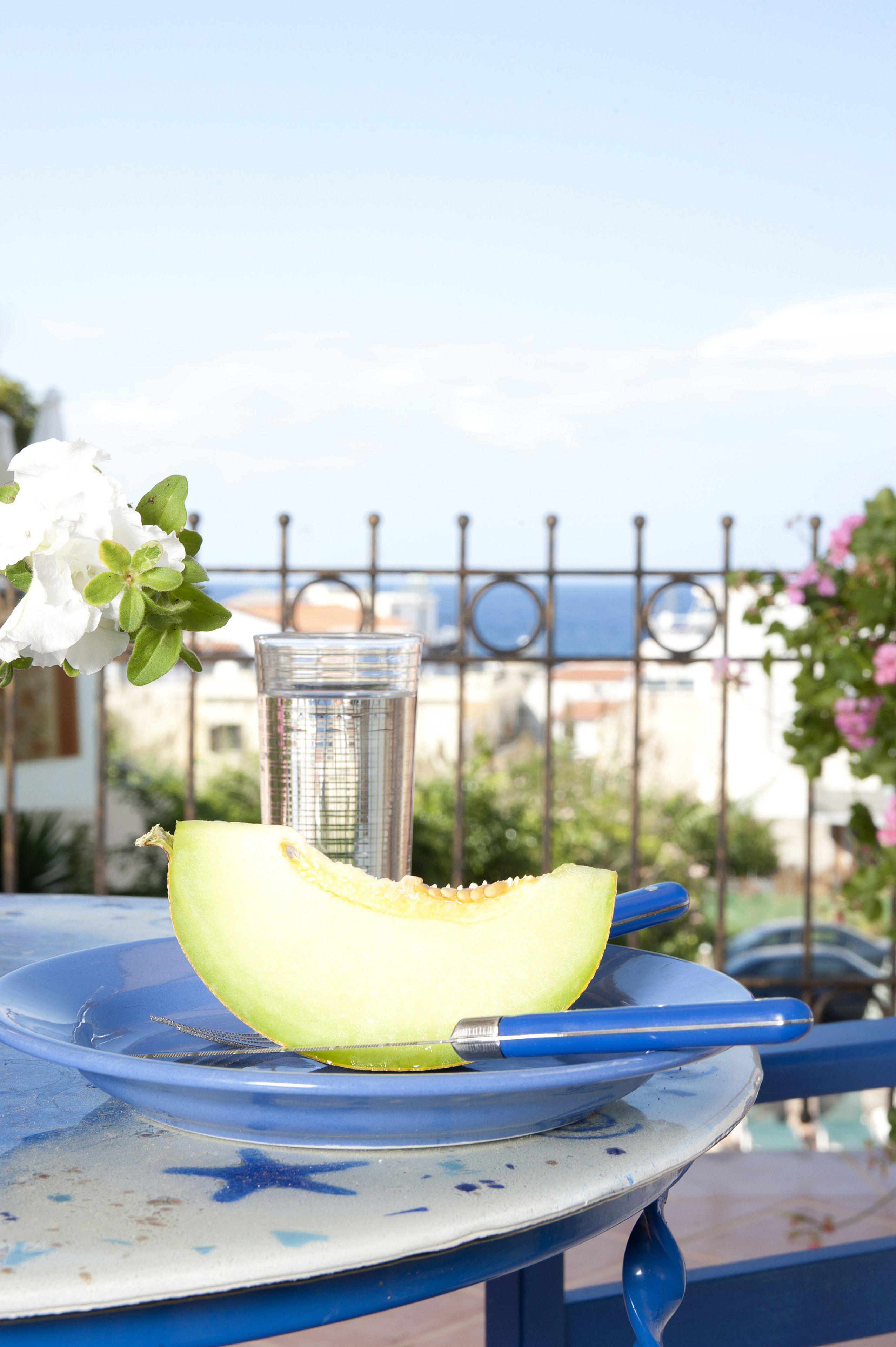 A table with a half-cut melon, a glass, and a blue-handled knife on a blue and white patterned tablecloth.