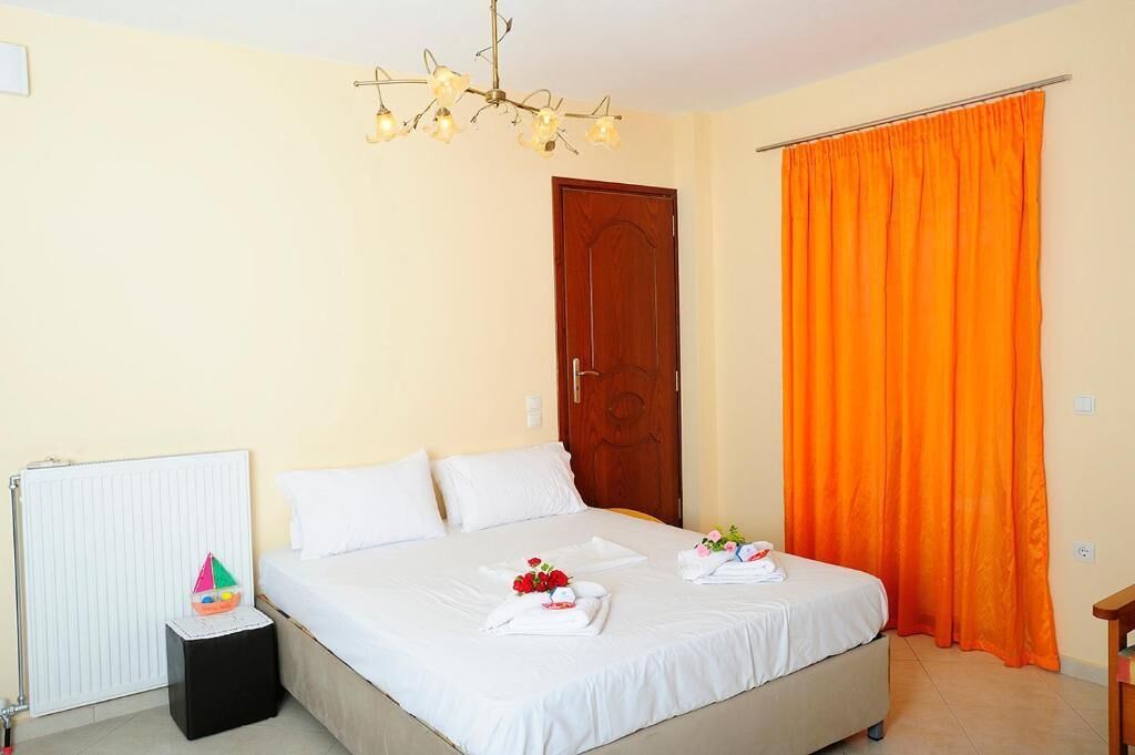 A neatly made bed with white linens, a wooden door, and an orange curtain.