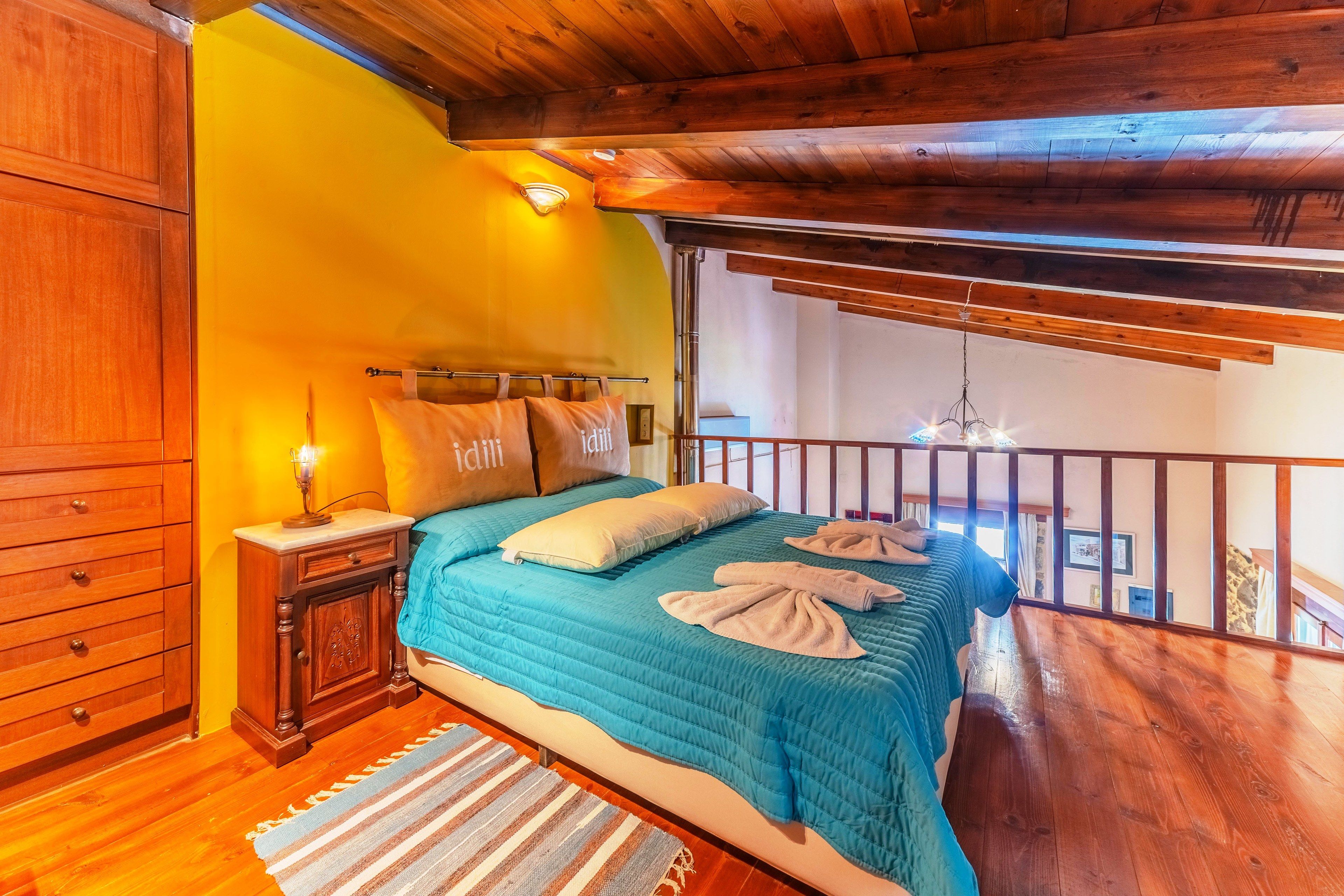 A bedroom with a wooden ceiling, a bed with blue bedding, a nightstand, and a view of a balcony.