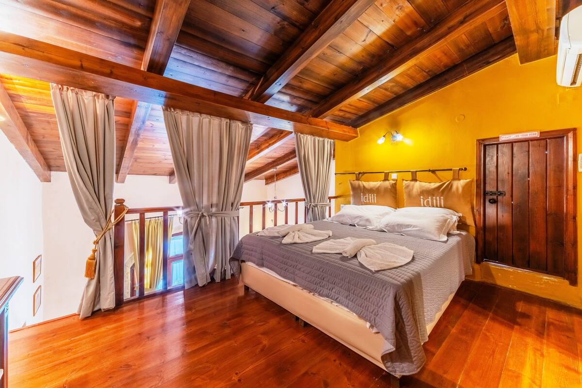 A bedroom with a wooden ceiling, a bed with towels, a balcony, and a door with a sign.