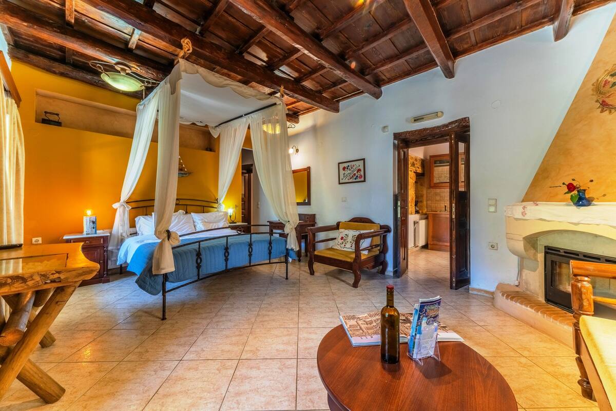 A bedroom with a canopy bed, wooden furniture, a fireplace, and a dining area.