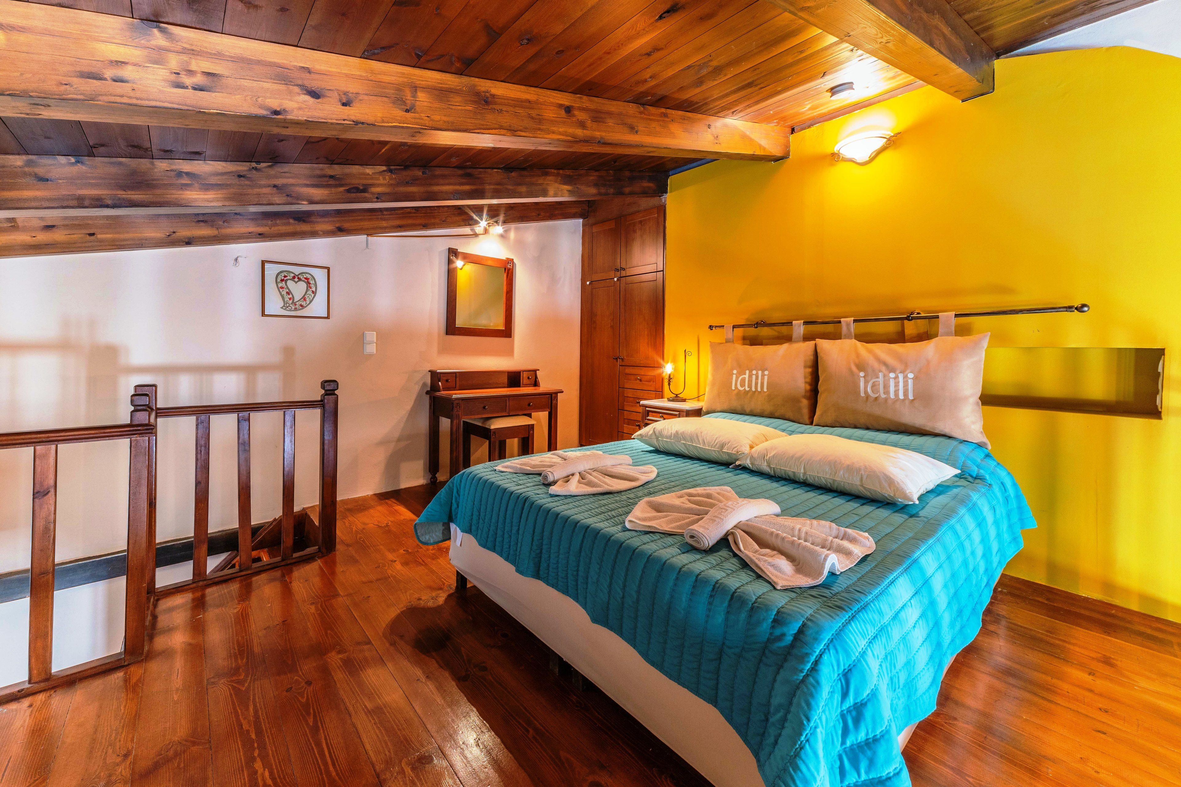 Een slaapkamer met een houten plafond, een bed met een blauwgroene sprei en een gele muur.