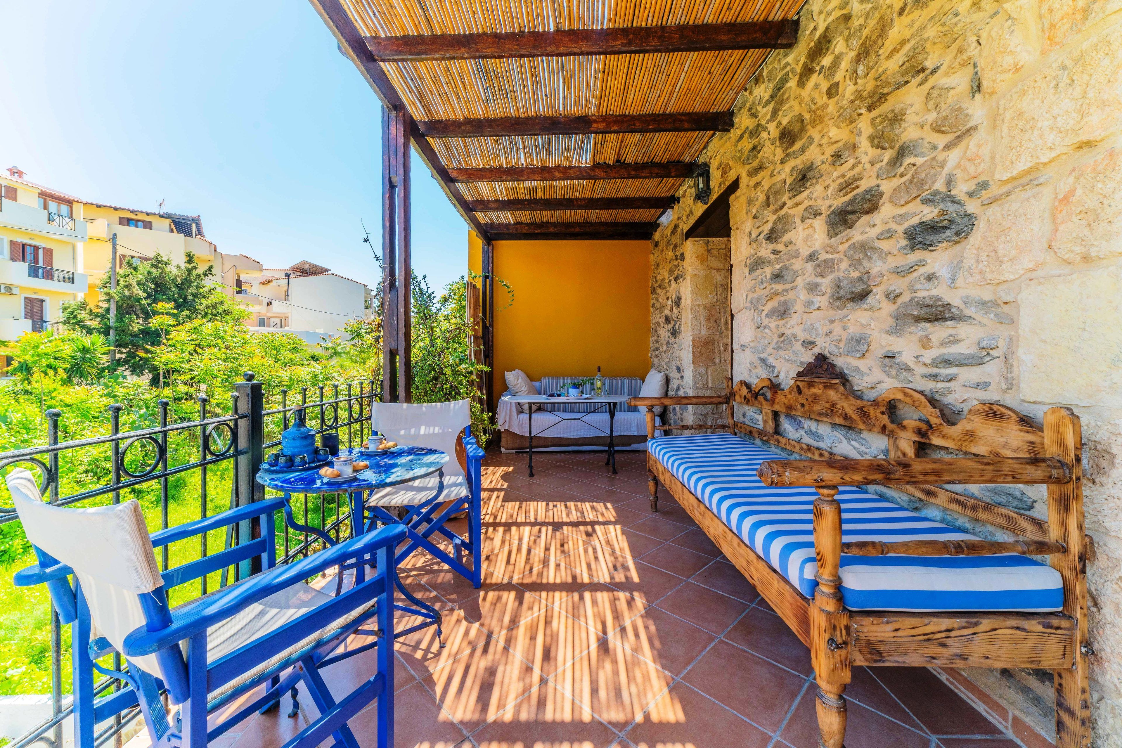A balcony with a wooden bench, a table, and blue chairs.
