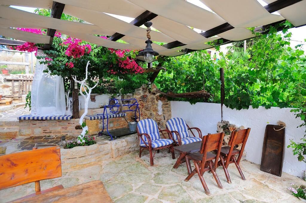 Eine Terrasse im Freien mit Steinböden, Holzstühlen, einer Bank und einer Pergola mit hängender Lampe.