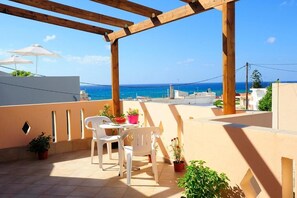 A terrace with a wooden pergola, white plastic chairs, a table, potted plants, and a view of the sea. - Idili Traditional House (Mylopotamos)