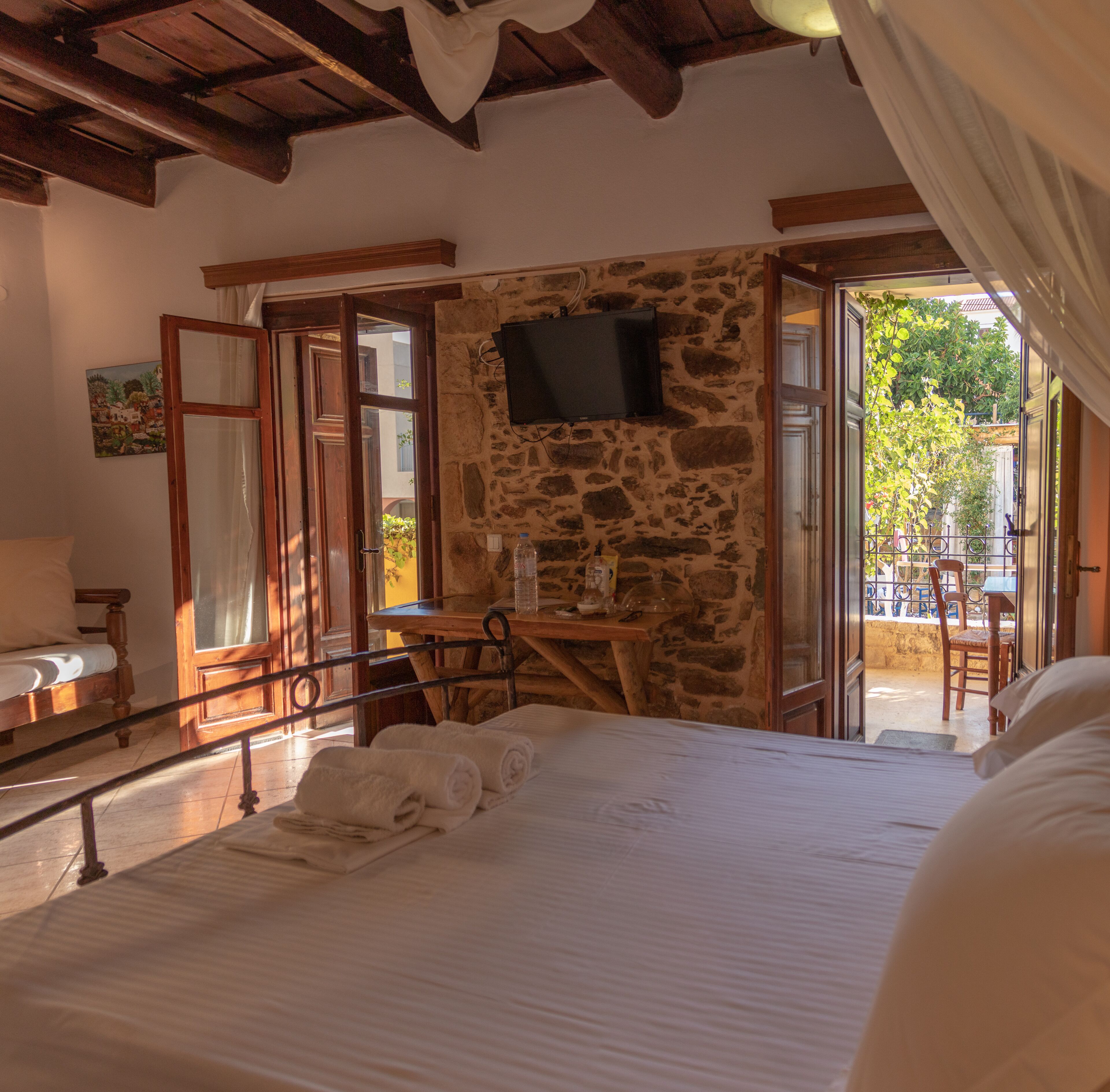 Una camera da letto con parete in pietra, letto con lenzuola bianche, una scrivania in legno e un televisore a parete.