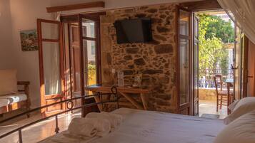 A bedroom with a stone wall, a bed with white linens, a wooden desk, and a television mounted on the wall.