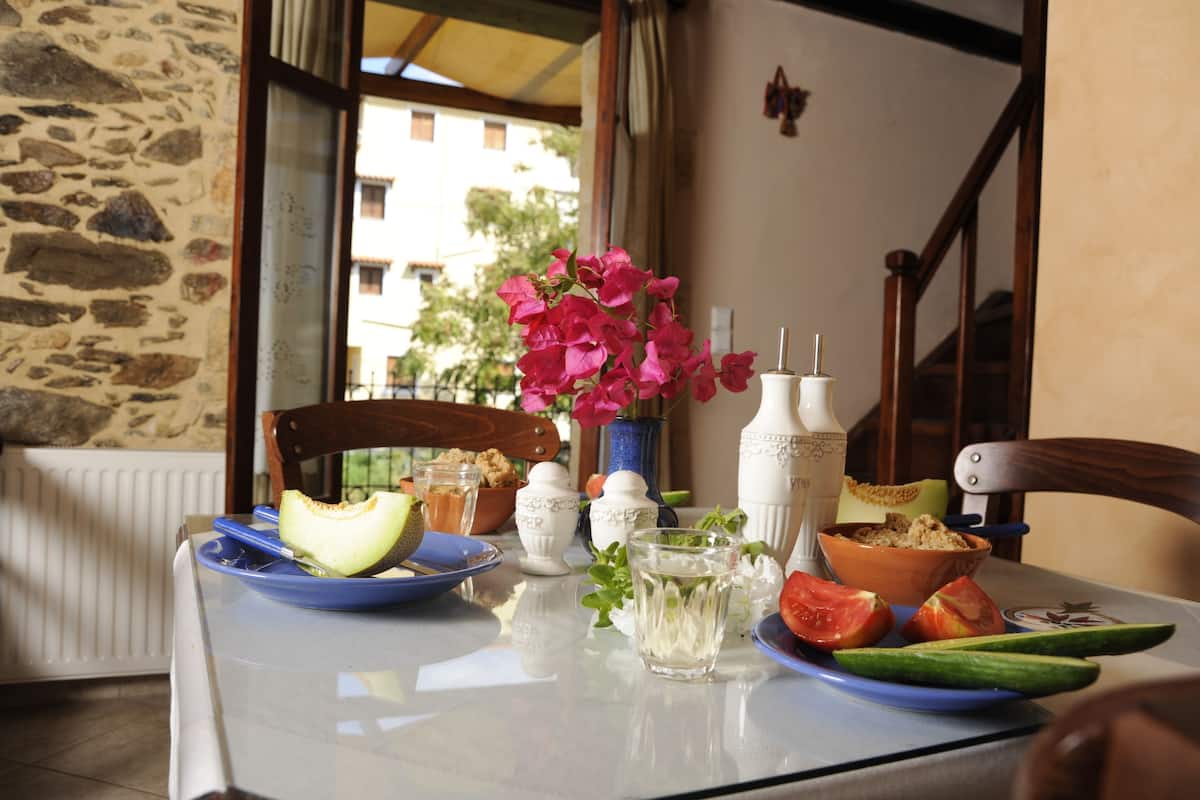 A table with a plate of melon, a bowl of cereal, a glass of water, and a vase with flowers.
