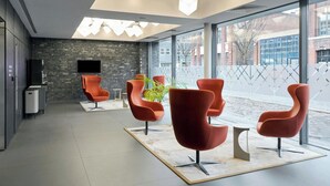 A modern waiting area with red chairs, a flat-screen TV, and a large window offering a view of the street. - Four Points Flex by Sheraton Birmingham Jewellery Quarter (Birmingham)