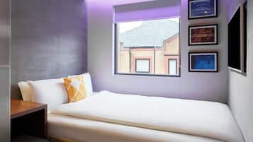 A modern bedroom with a bed, a nightstand, and a window with a cityscape view.