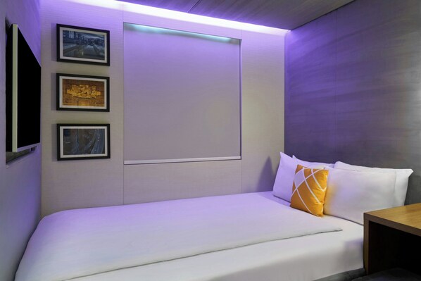 Una habitación de hotel moderna con una cama grande, un televisor de pantalla plana montado en la pared y tres cuadros enmarcados sobre la cama.