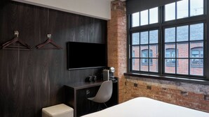 A modern hotel room with a large bed, a desk with a chair, a flat-screen TV mounted on the wall, and a window overlooking a brick building. - Four Points Flex by Sheraton Birmingham Jewellery Quarter (Birmingham)