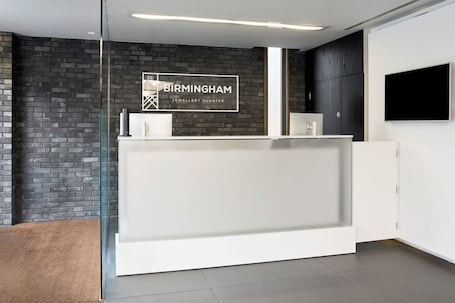 A reception area with a glass partition, a reception desk, a black brick wall, and a mounted television.