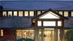 A hotel entrance with a brick facade, a glass entrance, and a cobblestone driveway. - Aspria Royal La Rasante (Brussels)