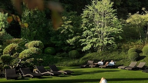 A serene outdoor lounge area with multiple lounge chairs arranged on a well-manicured lawn, surrounded by lush greenery and neatly trimmed bushes. - Aspria Royal La Rasante (Brussels)