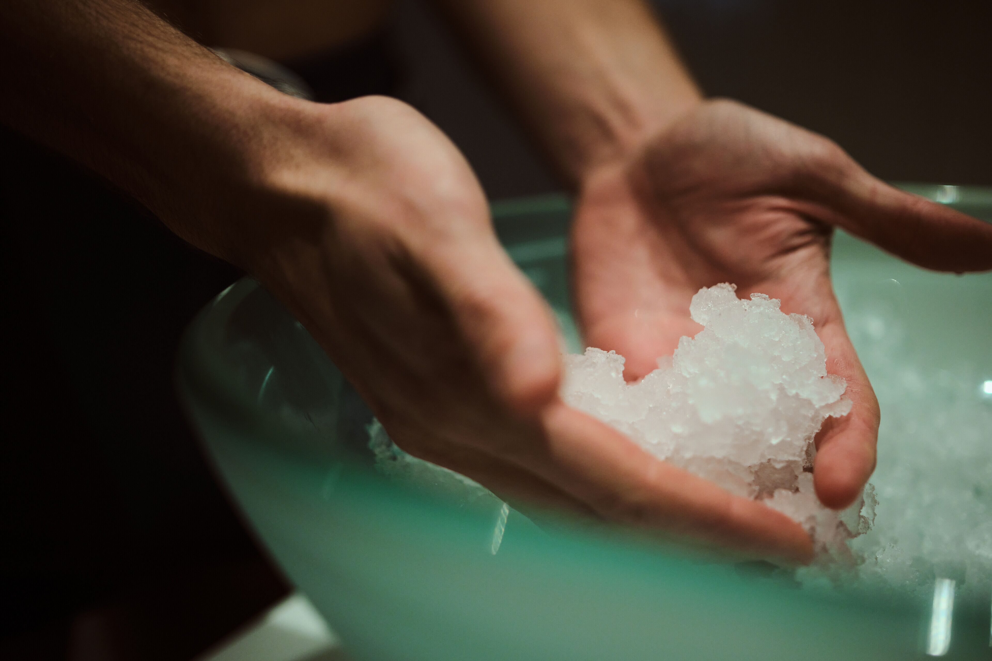 Hände halten Eiswürfel in einer Schüssel.