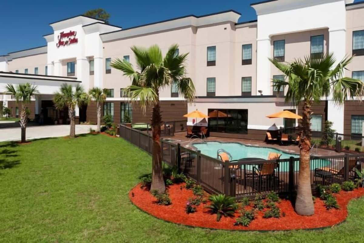 A hotel with a swimming pool, palm trees, and outdoor seating.