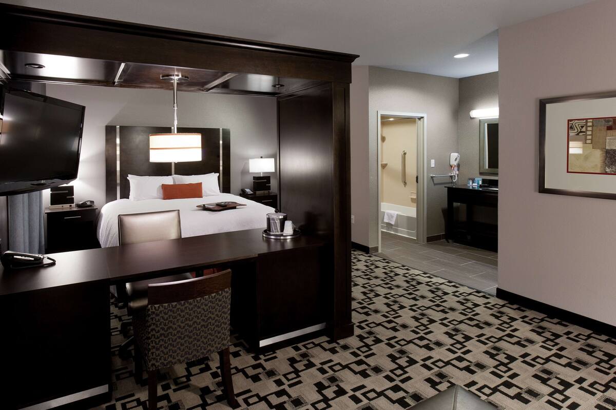 A hotel room with a bed, desk, chair, and a TV.