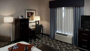 Een hotelkamer met een bed, bureau, stoel, lamp, televisie en een kamer met een patroon op de vloer.