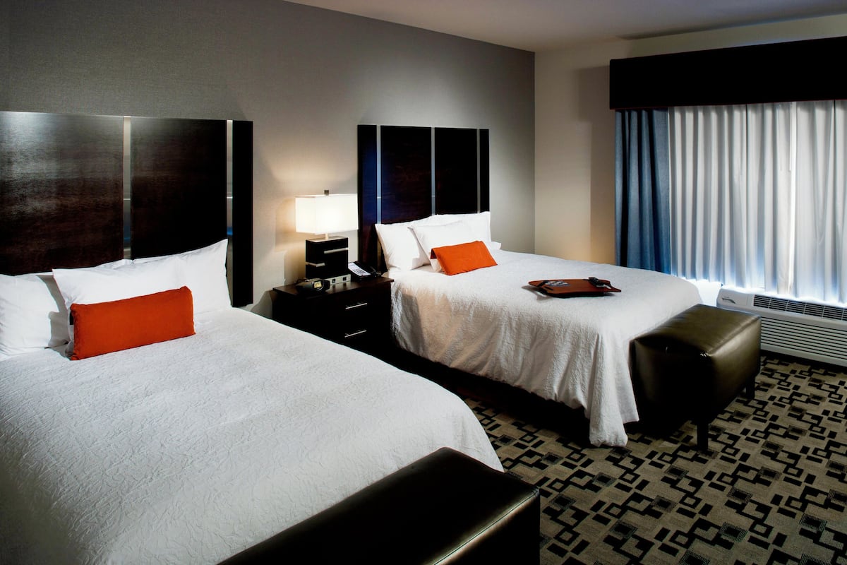 A hotel room with two beds, a nightstand with a lamp, a bench, and a patterned carpet.
