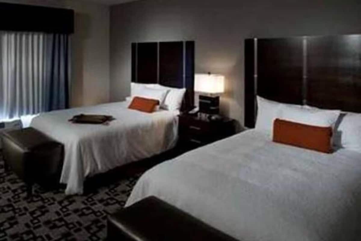 A hotel room with two beds, a nightstand with a lamp, and a patterned carpet.